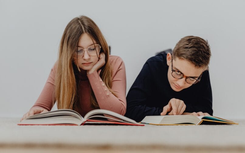 A young boy and a young girl wearing glasses while reading books